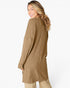 A woman wearing a long-sleeve ribbed knit tunic sweater in camel brown, shown from a side-back angle against a plain white studio background.