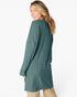 A woman wearing a ribbed knit long-sleeve tunic sweater in a muted teal green, shown from a three-quarters back view against a plain white studio background.