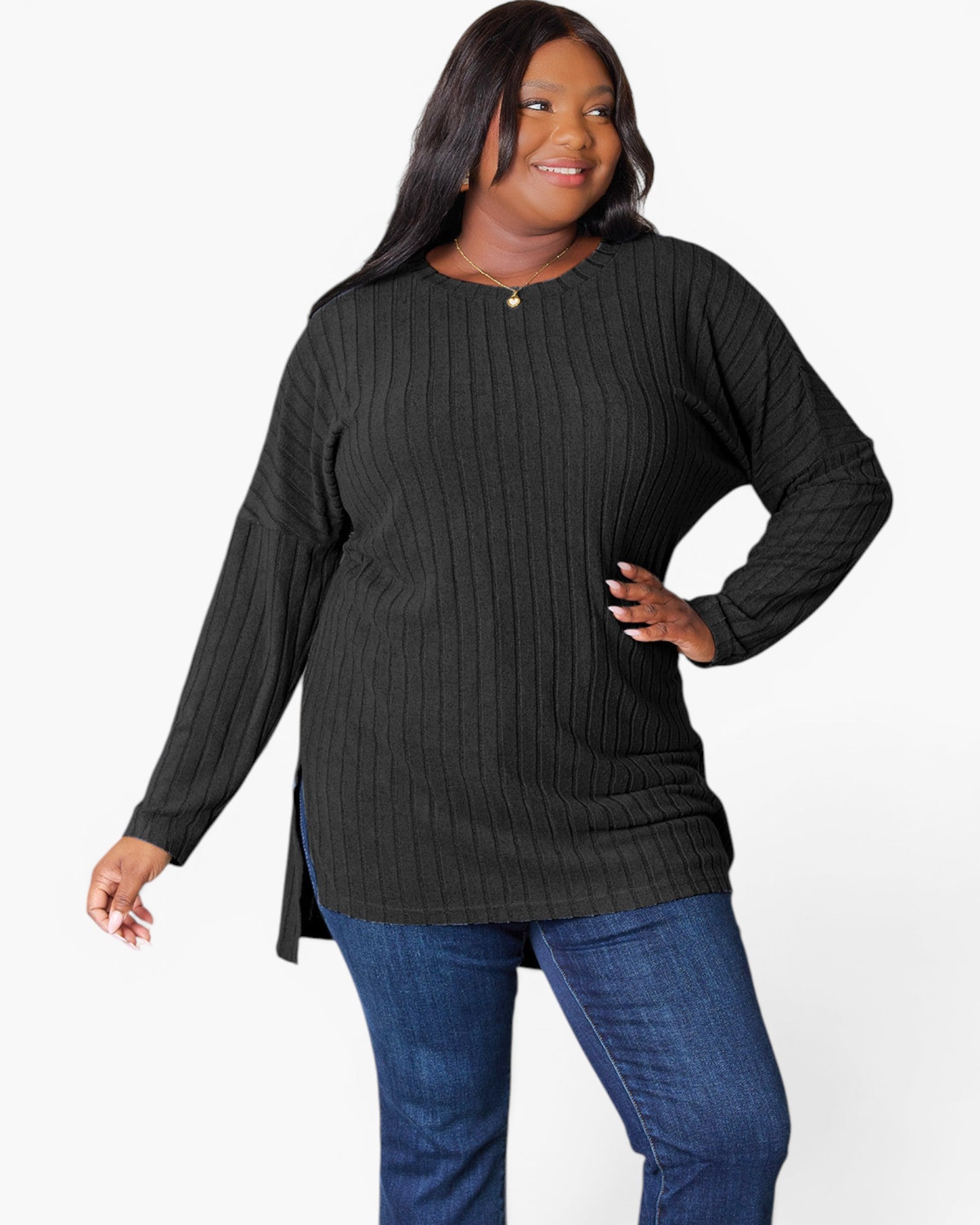 A woman modeling a black ribbed knit long-sleeve tunic top with a high-low hem, paired with blue jeans, against a plain white studio background.