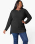 A woman modeling a black ribbed knit long-sleeve tunic top with a high-low hem, paired with blue jeans, against a plain white studio background.