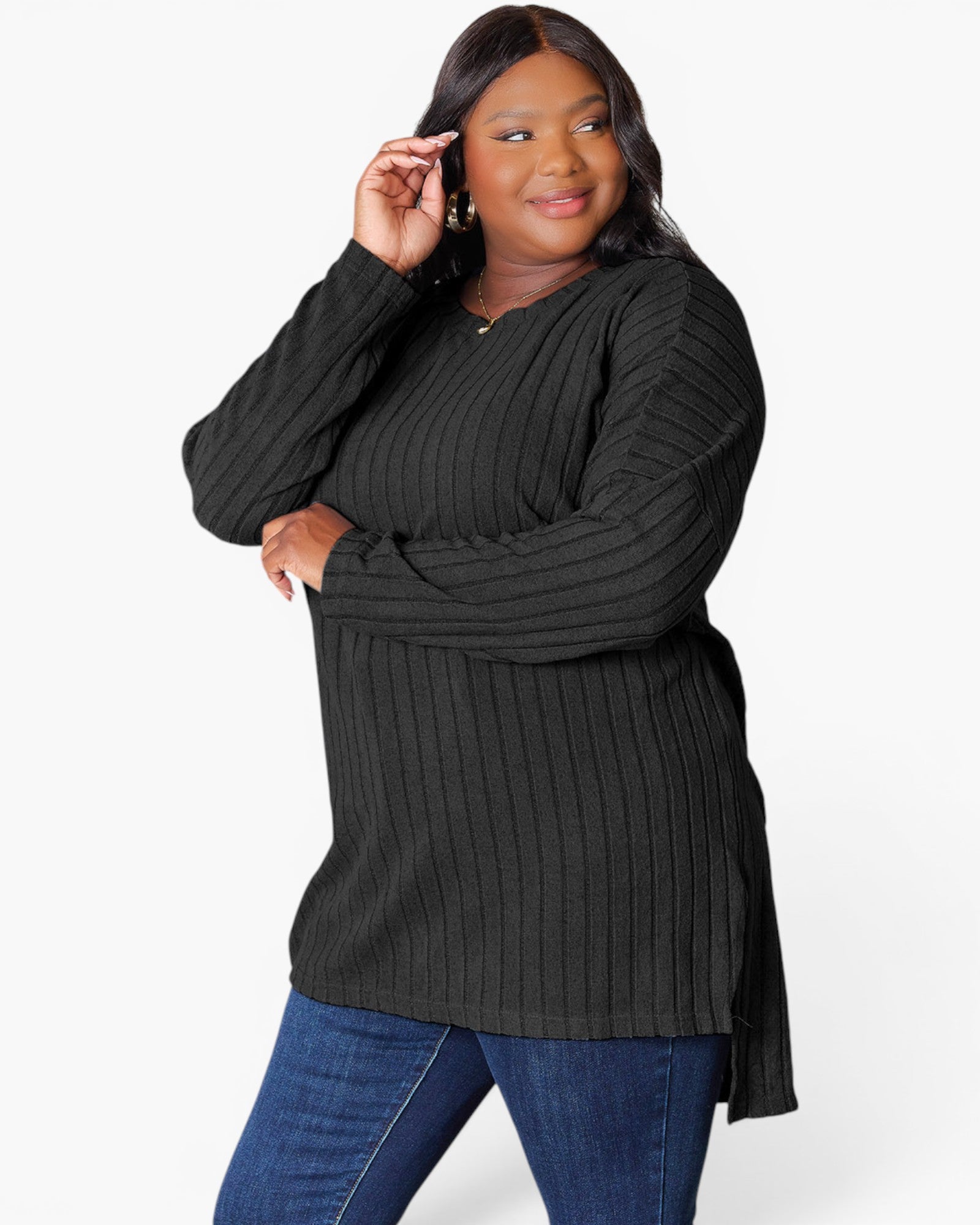 A woman modeling a black ribbed long-sleeve tunic top with blue jeans against a plain white studio background.