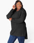 A woman modeling a black ribbed long-sleeve tunic top with blue jeans against a plain white studio background.