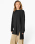 A woman wearing a black ribbed long-sleeve tunic top with a high-low hem and side slits, paired with beige pants, against a plain white studio background.
