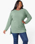 A plus-size woman wearing a sage green ribbed knit long-sleeve tunic top with blue jeans, posing against a solid white studio background.