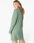 A woman wearing a sage green ribbed knit long-sleeve tunic sweater, shown from a side-back angle against a plain white studio background.