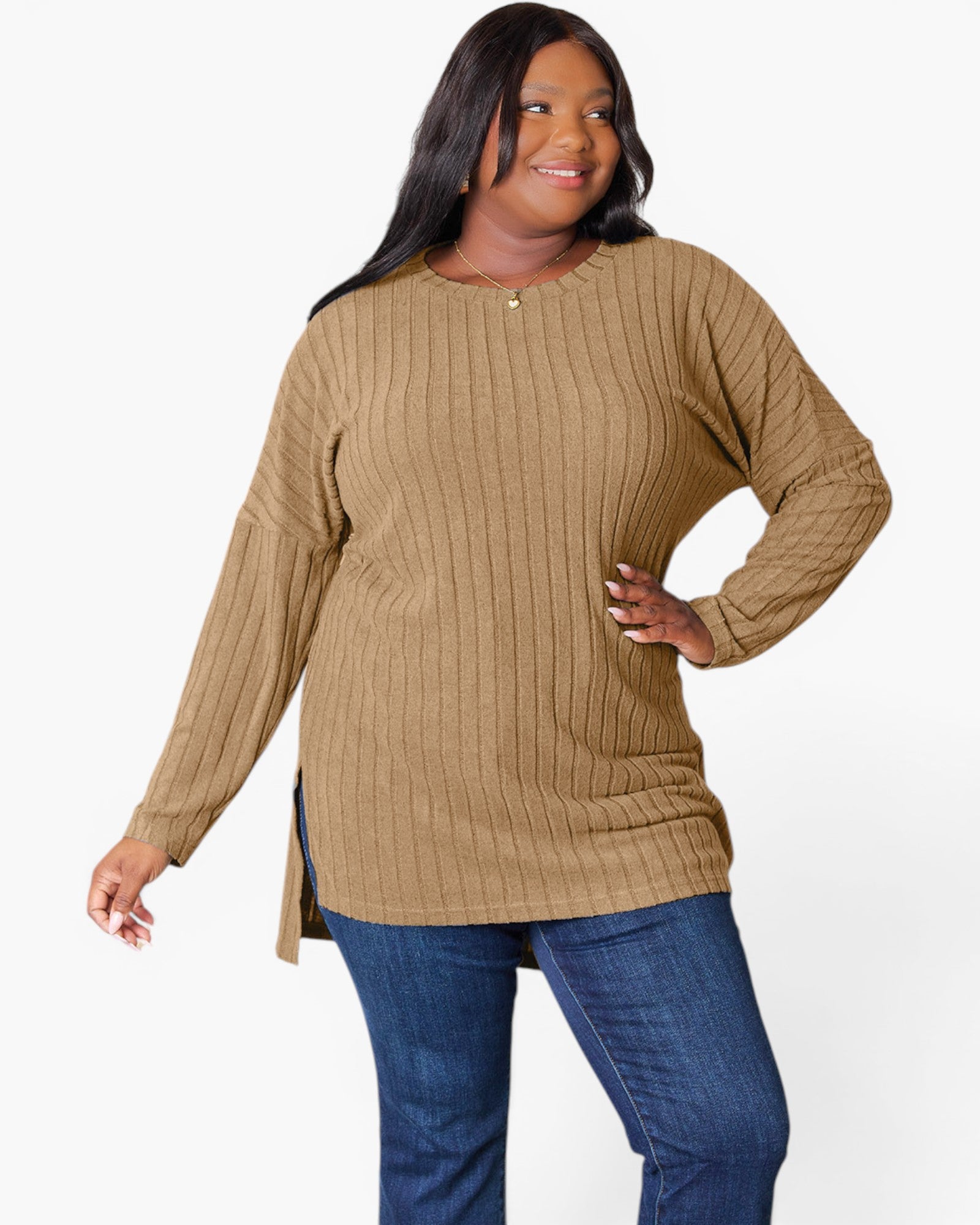 A woman modeling a ribbed knit long-sleeve tunic top in camel brown, paired with blue jeans, against a plain white studio background.