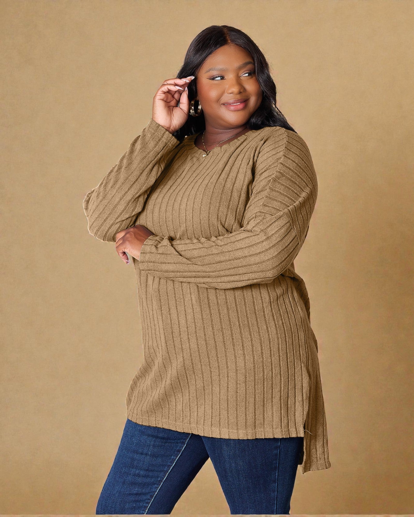 Woman wearing a ribbed brown sweater and blue jeans against a beige background