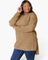 A woman modeling a ribbed knit long-sleeve tunic top in camel brown, paired with blue jeans, against a plain white studio background.