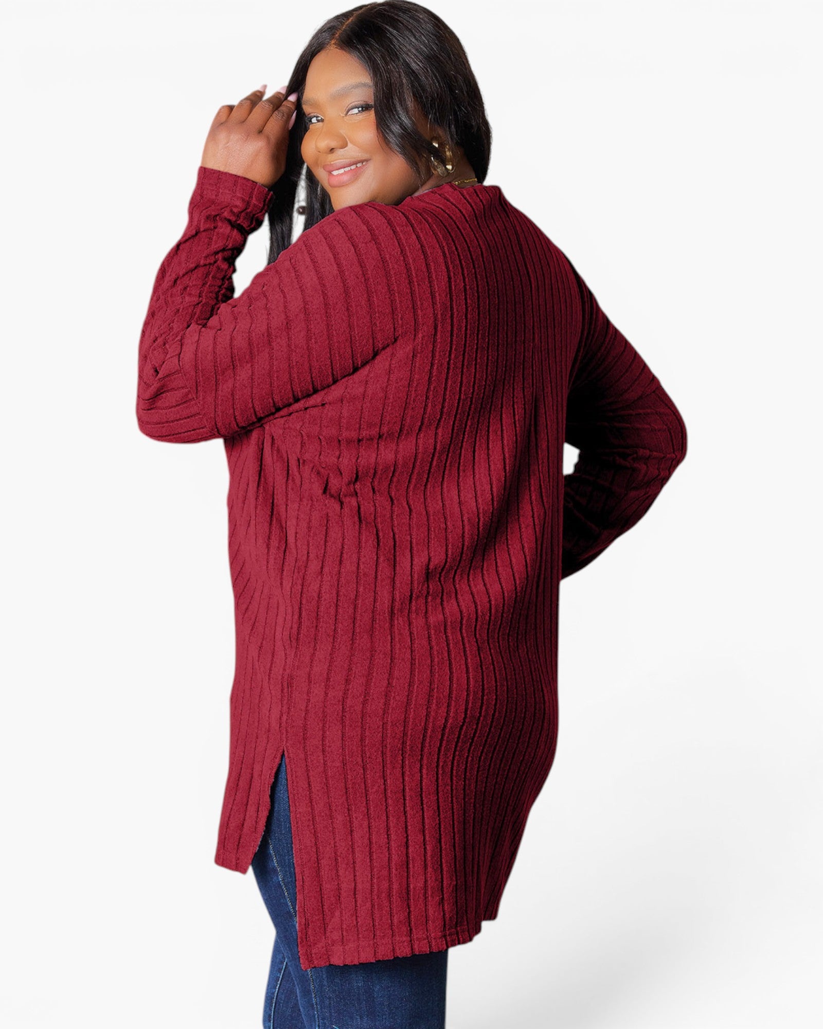 A woman wearing a ribbed knit long-sleeve tunic sweater in deep burgundy, shown from a three-quarters back view against a light gray studio background.