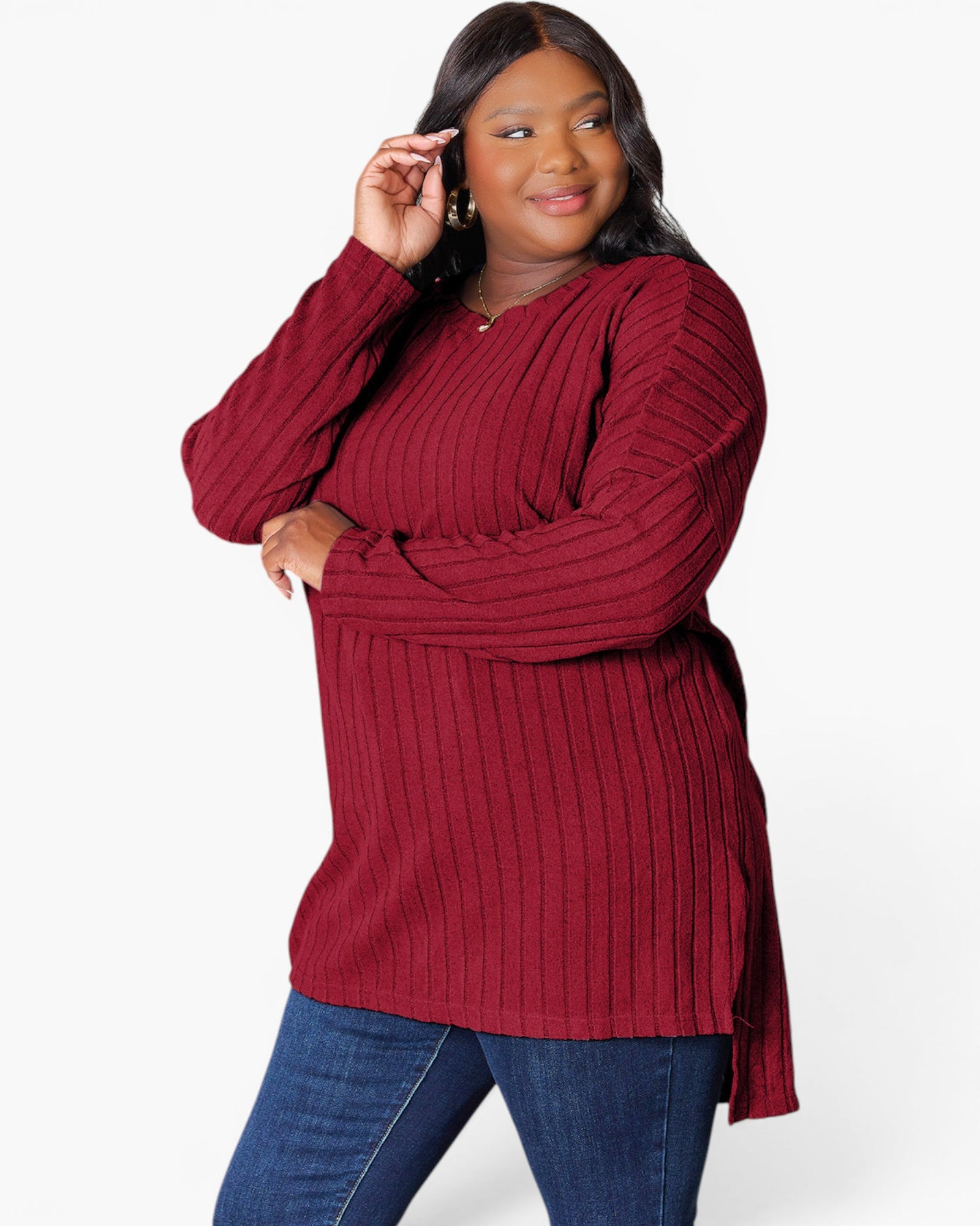 A woman modeling a ribbed knit long-sleeve tunic top in deep burgundy, paired with blue jeans, against a plain white studio background.