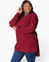 A woman modeling a ribbed knit long-sleeve tunic top in deep burgundy, paired with blue jeans, against a plain white studio background.