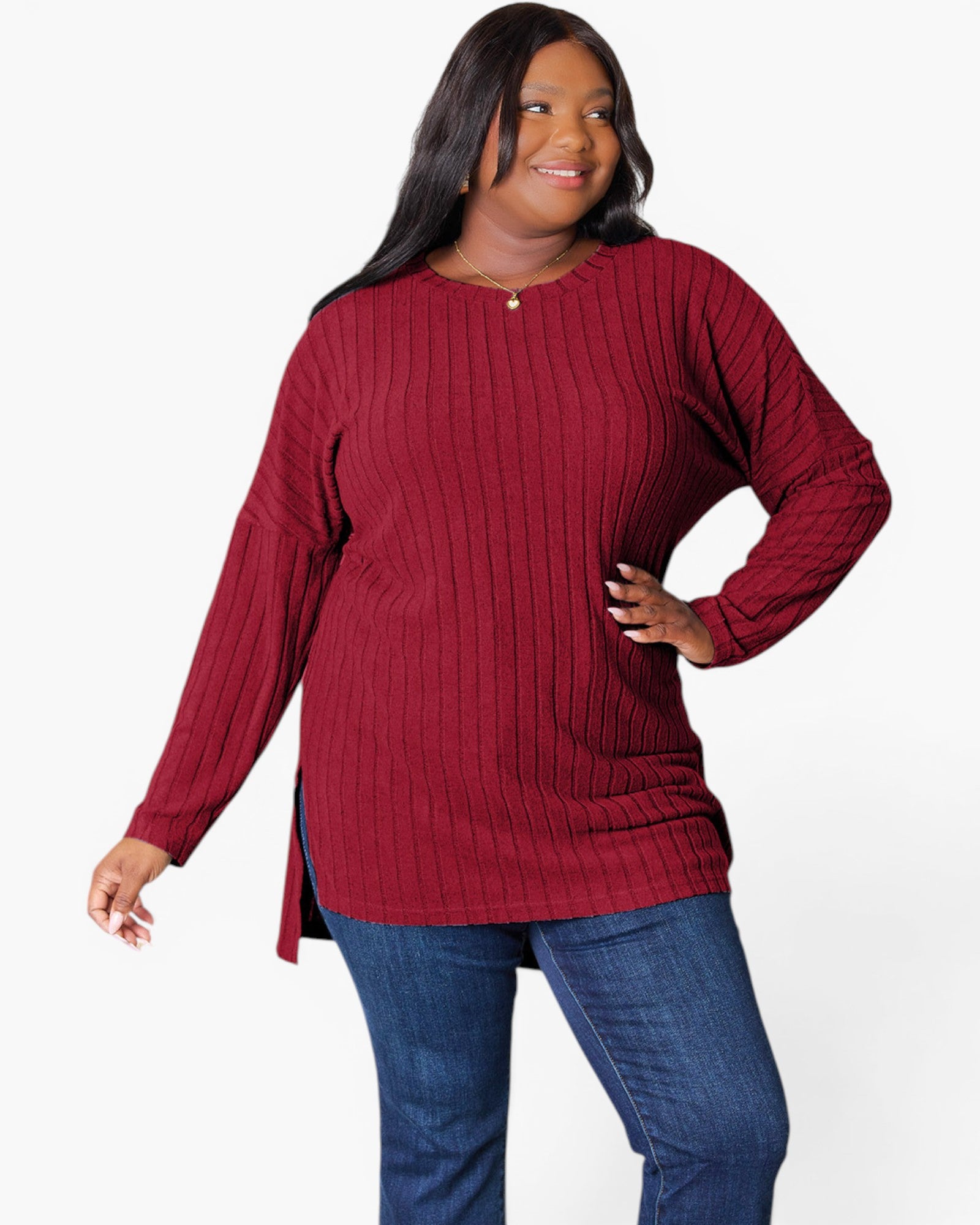 A woman modeling a long-sleeve ribbed knit tunic top in deep burgundy, paired with blue jeans, against a plain white studio background.
