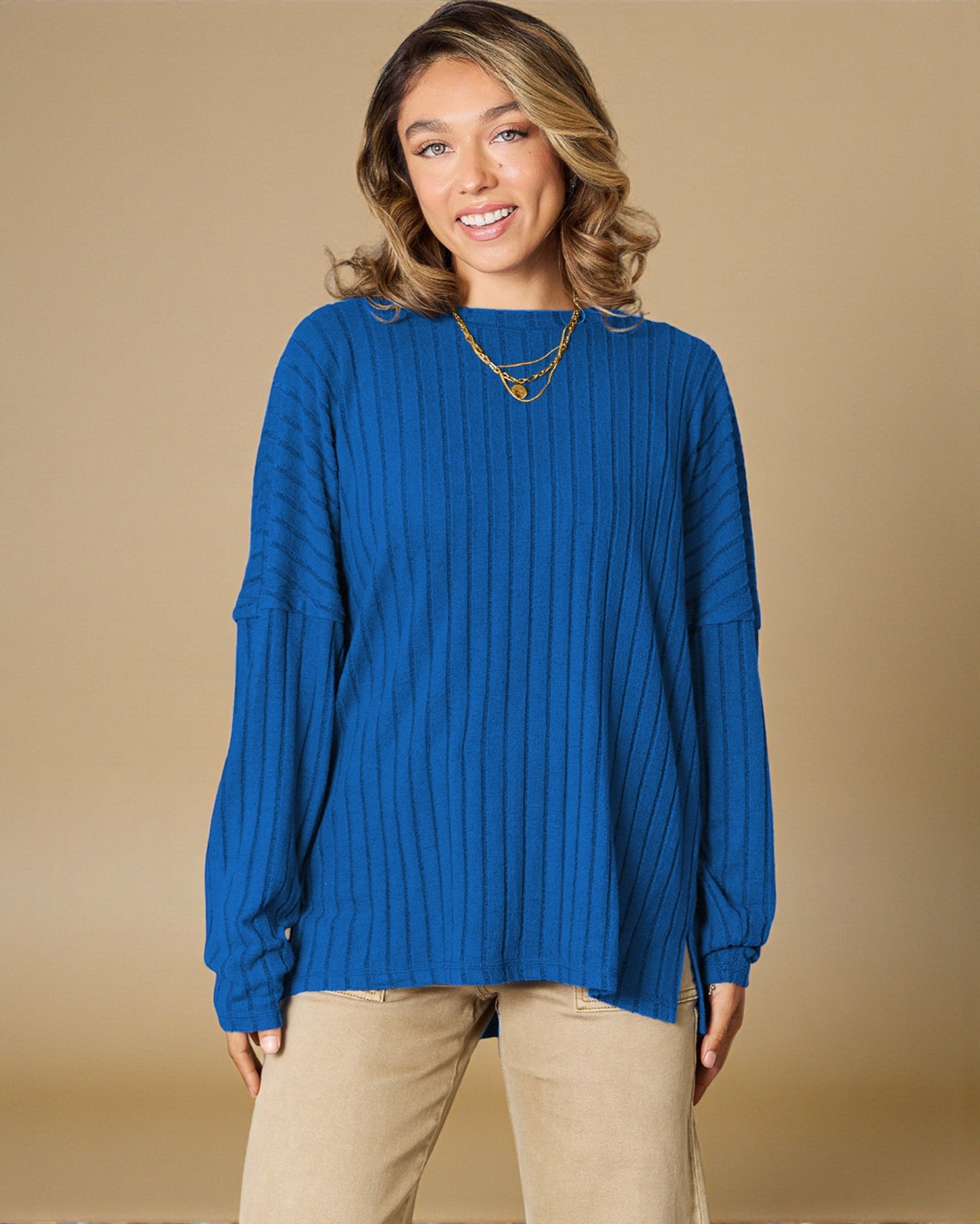 Woman wearing a blue sweater and beige pants against a beige background