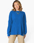 A woman wearing a royal blue ribbed knit long-sleeve top and beige pants, standing against a plain white studio background.