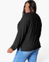 A woman wearing a black ribbed knit long-sleeve top and blue jeans, photographed from the back against a plain white studio background.