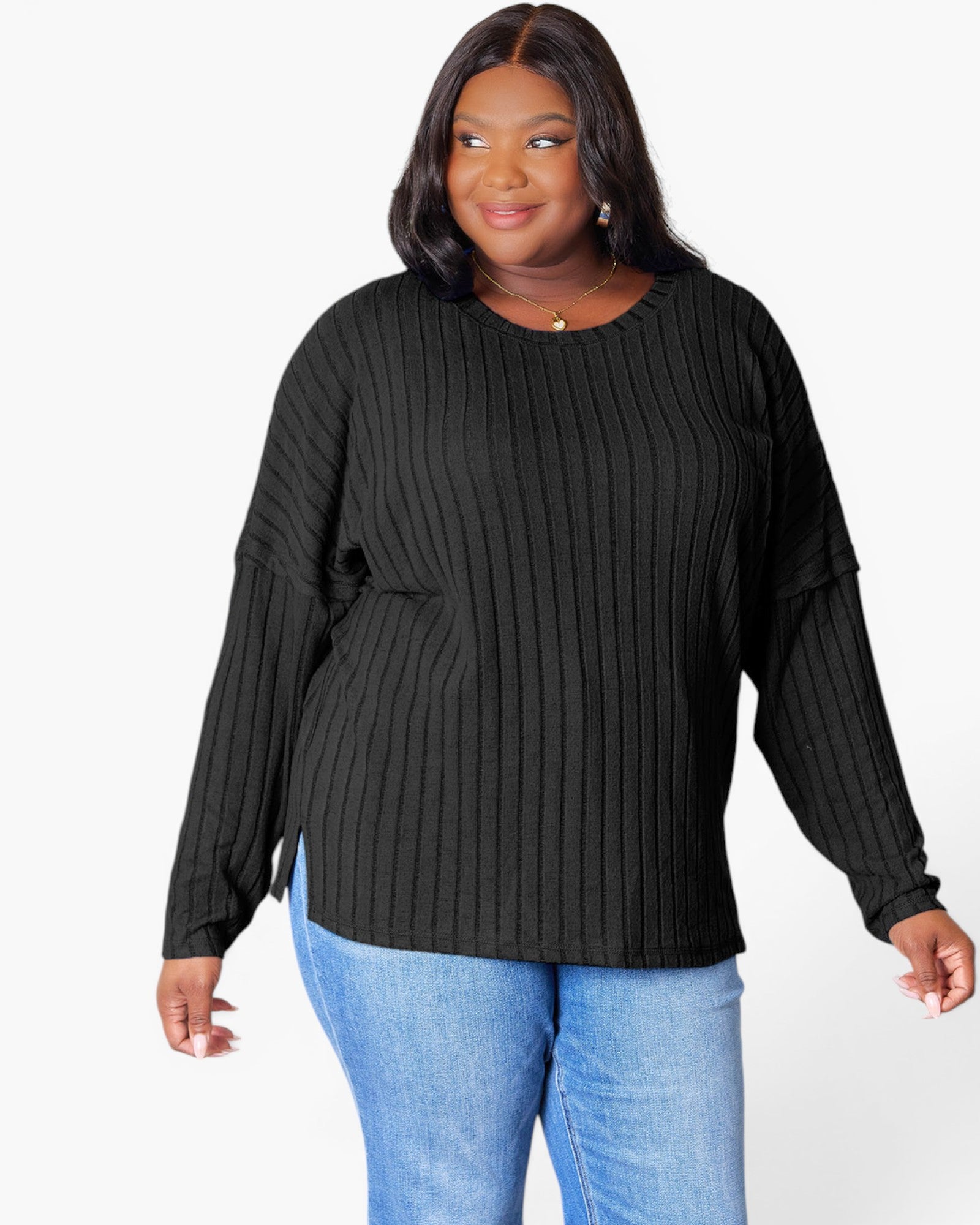A woman wearing a black ribbed knit long-sleeve top with a crew neck and side slits, paired with blue jeans, against a plain white background.