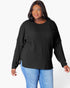 A woman wearing a black ribbed knit long-sleeve top with a crew neck and side slits, paired with blue jeans, against a plain white background.