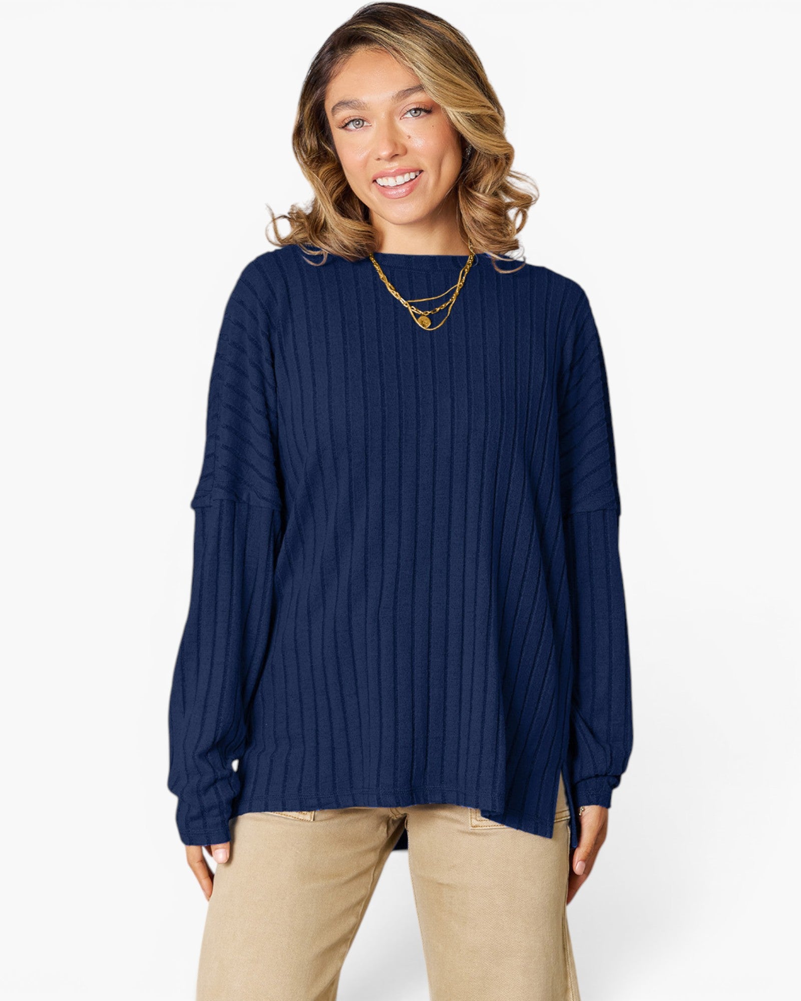 A woman wearing a navy blue ribbed knit long-sleeve top and beige pants, standing against a plain white studio background.
