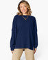 A woman wearing a navy blue ribbed knit long-sleeve top and beige pants, standing against a plain white studio background.