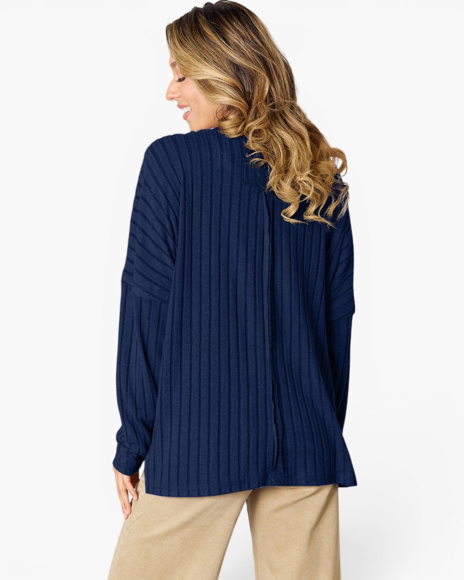 A woman shown from the back wearing a navy blue ribbed knit sweater and beige pants against a light gray studio background.