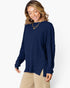 A woman wearing a navy blue ribbed knit long-sleeve sweater and beige pants, standing against a plain white studio background.