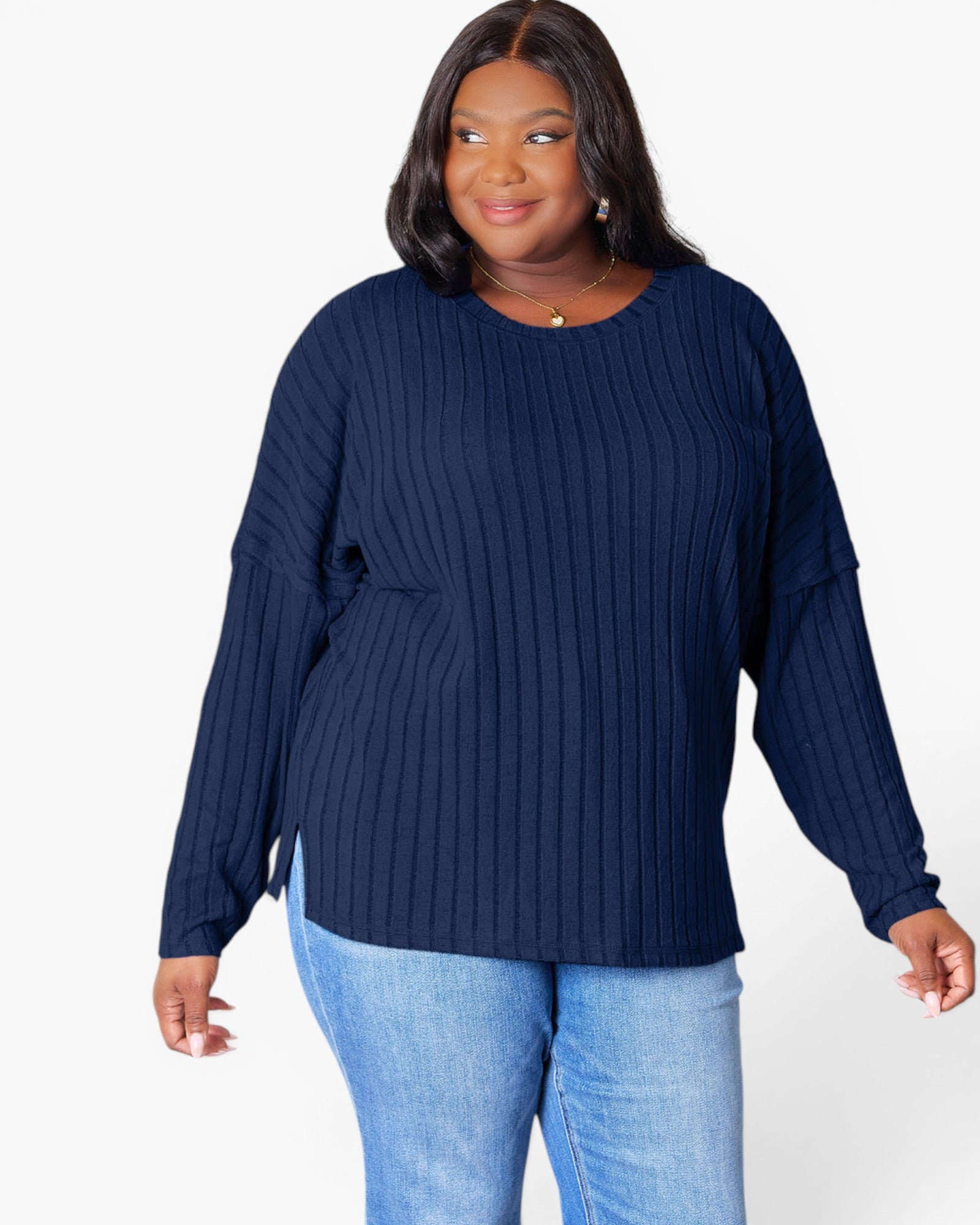 A woman modeling a navy blue ribbed knit long-sleeve top with a crew neck and side slits, paired with light blue jeans, against a plain white background.
