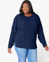 A woman modeling a navy blue ribbed knit long-sleeve top with a crew neck and side slits, paired with light blue jeans, against a plain white background.