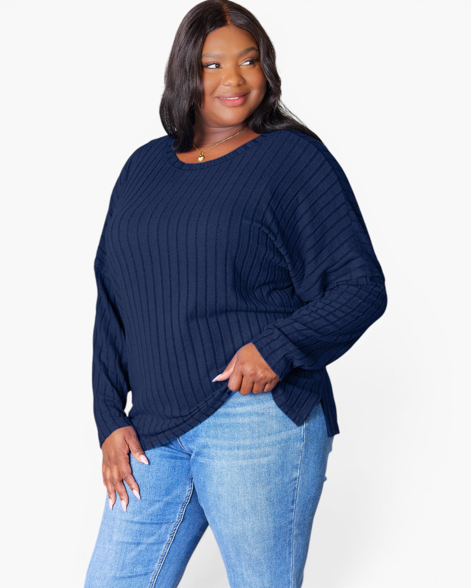 A woman modeling a navy blue ribbed knit sweater with long balloon sleeves, paired with light blue jeans, against a plain white studio background.