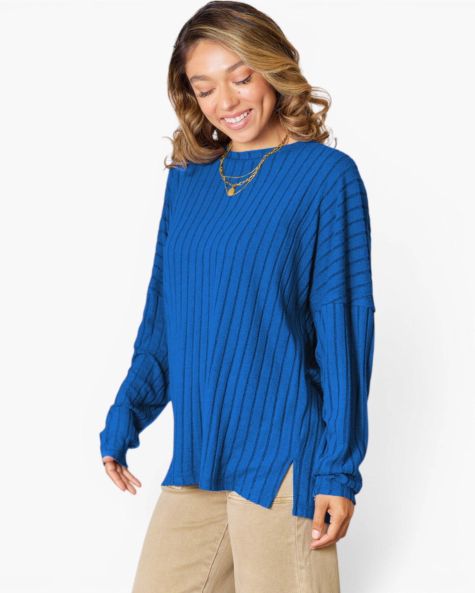 A woman wearing a vibrant royal blue ribbed knit sweater with long balloon sleeves and a side slit hem, paired with beige pants, against a plain white studio background.