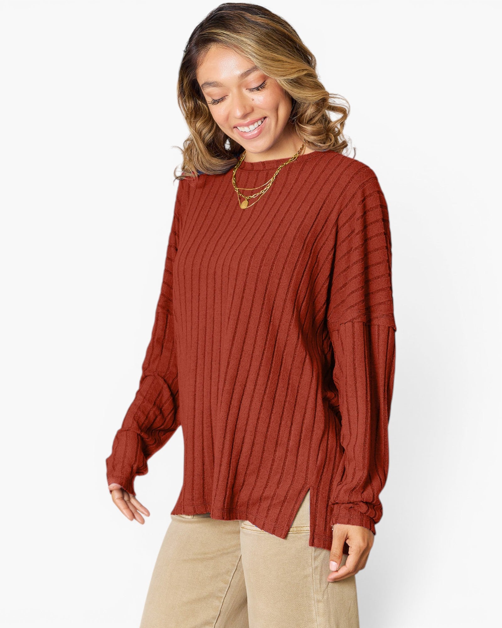 A woman wearing a rust-colored ribbed knit long-sleeve top and beige pants, standing against a plain white studio background.