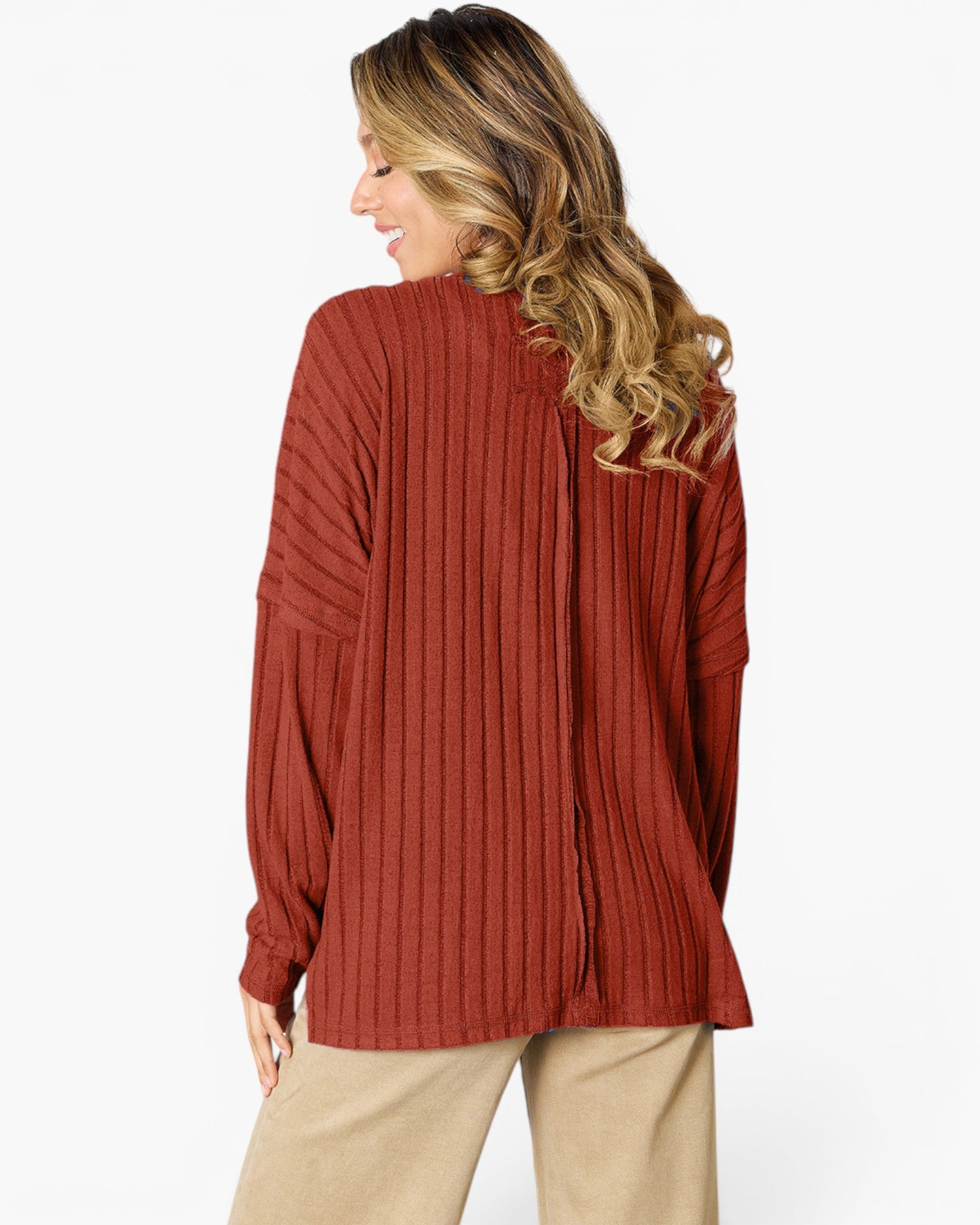 A woman shown from the back wearing a rust-colored ribbed knit sweater and beige pants against a plain white background.