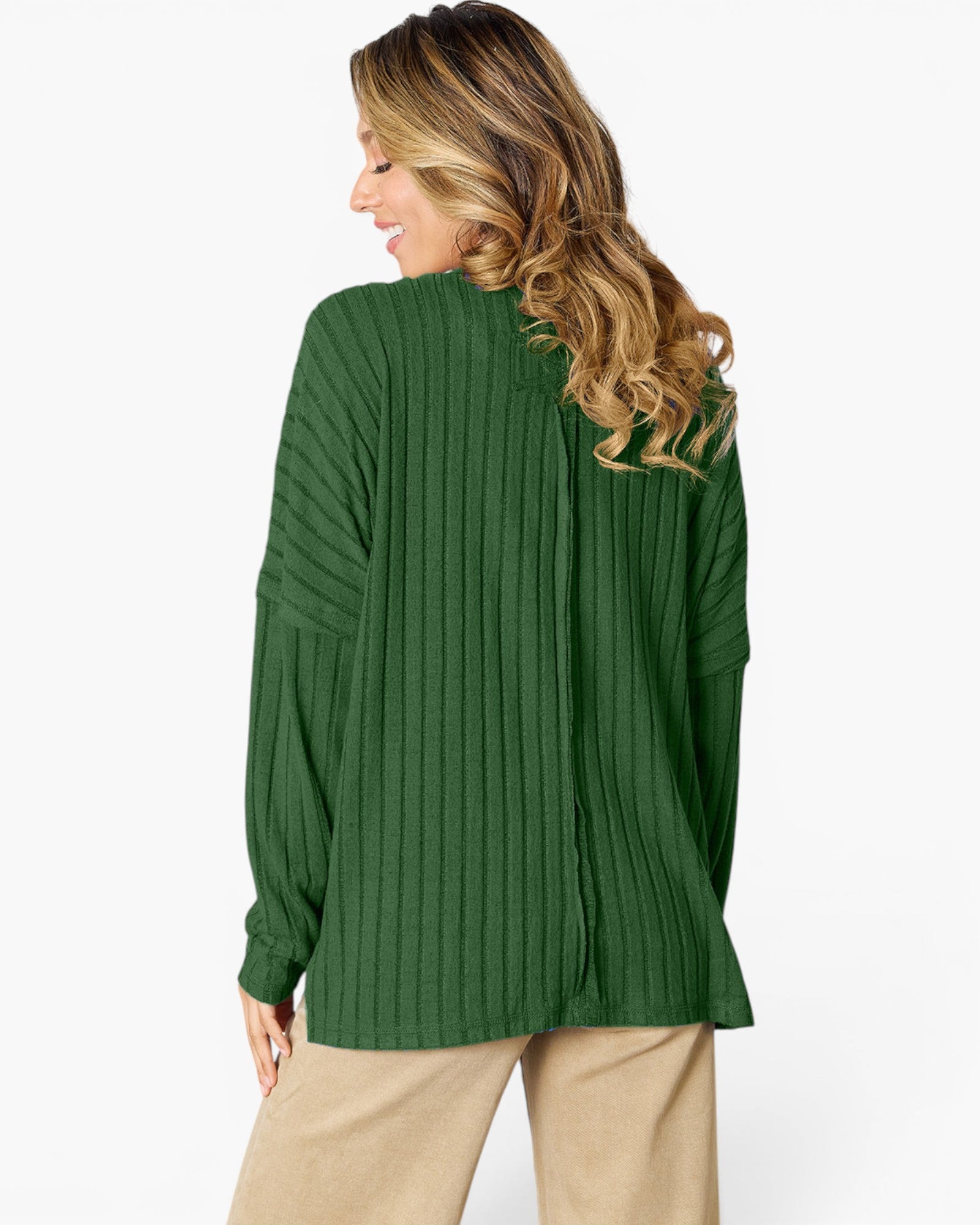 A woman shown from the back wearing a dark green ribbed knit sweater and beige pants against a plain white studio background.