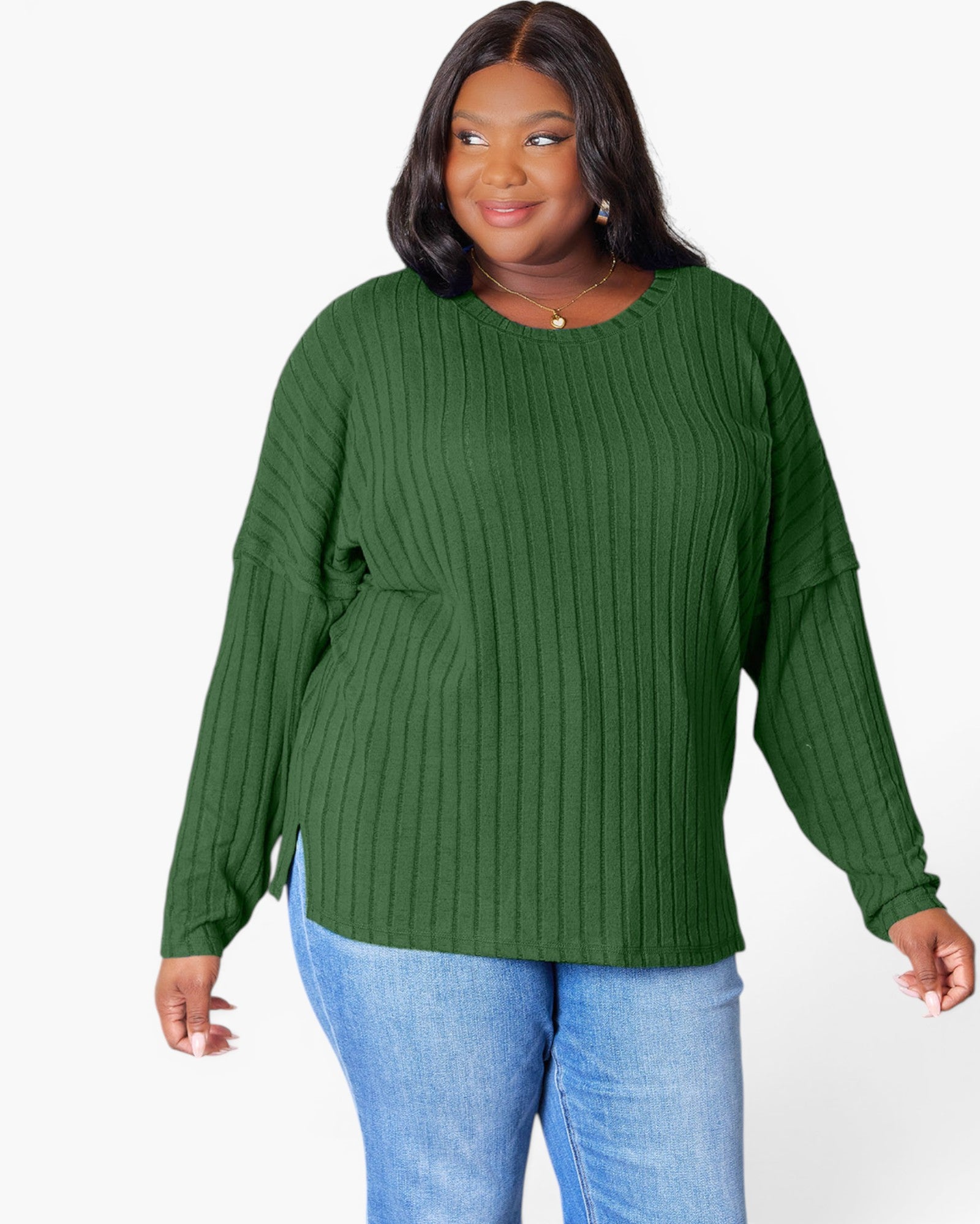 A woman wearing a green ribbed knit long-sleeve top with a crew neck and side pockets, paired with blue jeans, against a plain white background.