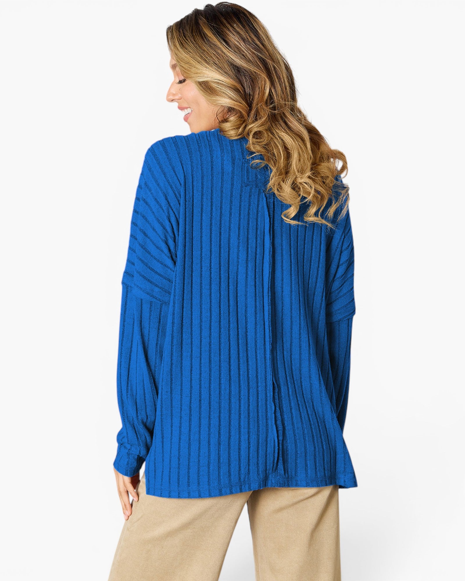 A woman shown from the back wearing a bright blue ribbed knit sweater and beige pants against a plain white studio background.