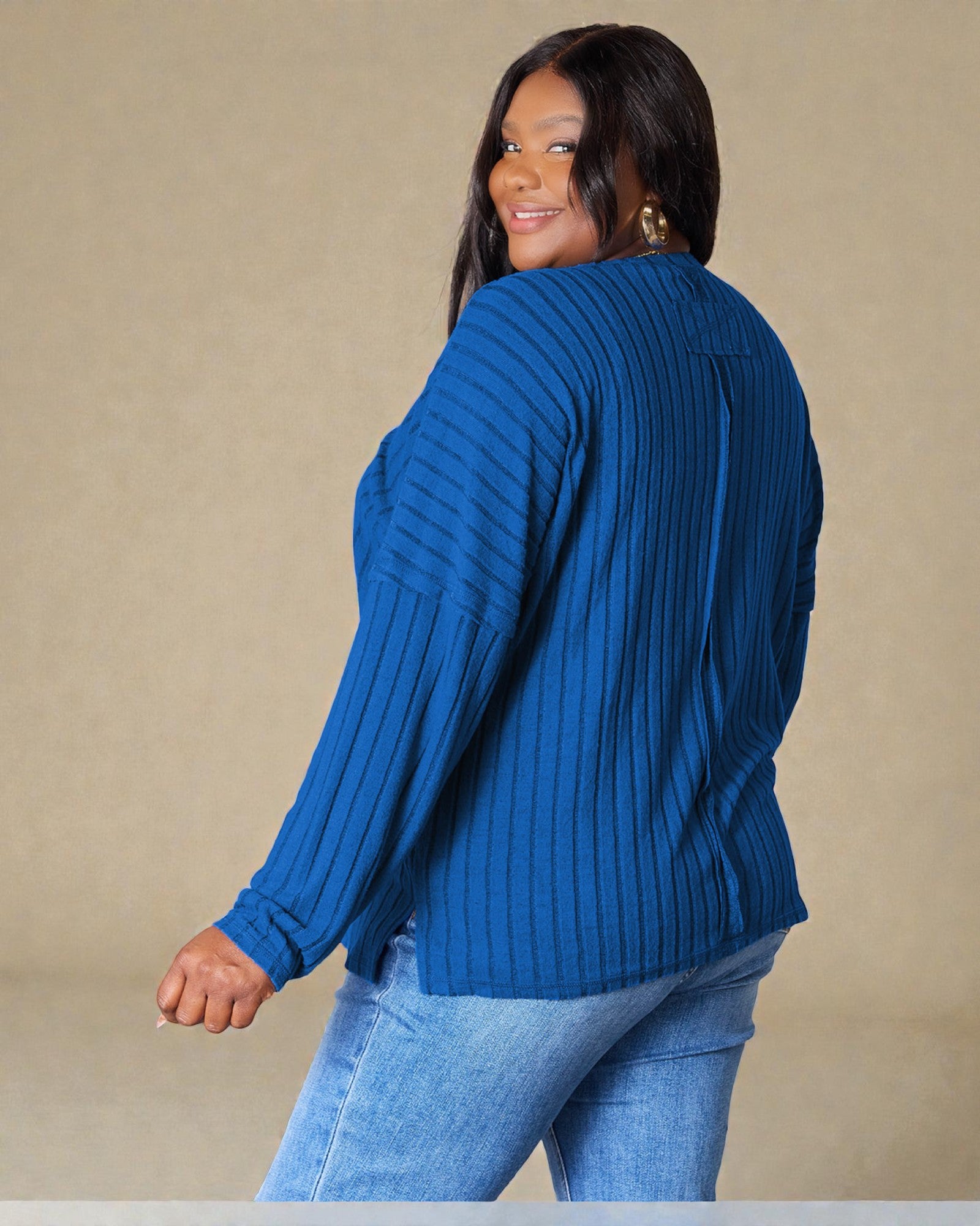 Woman wearing a blue ribbed sweater and jeans against a beige background