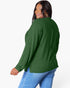 A woman wearing a dark green ribbed knit sweater and blue jeans, shown from a three-quarters back view against a plain white background.