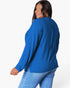 A woman wearing a bright blue ribbed knit long-sleeve top and light blue jeans, shown from a three-quarters back view against a plain white studio background.