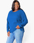 A woman modeling a bright blue ribbed knit sweater with long sleeves and a relaxed fit, paired with light blue jeans, against a plain white studio background.