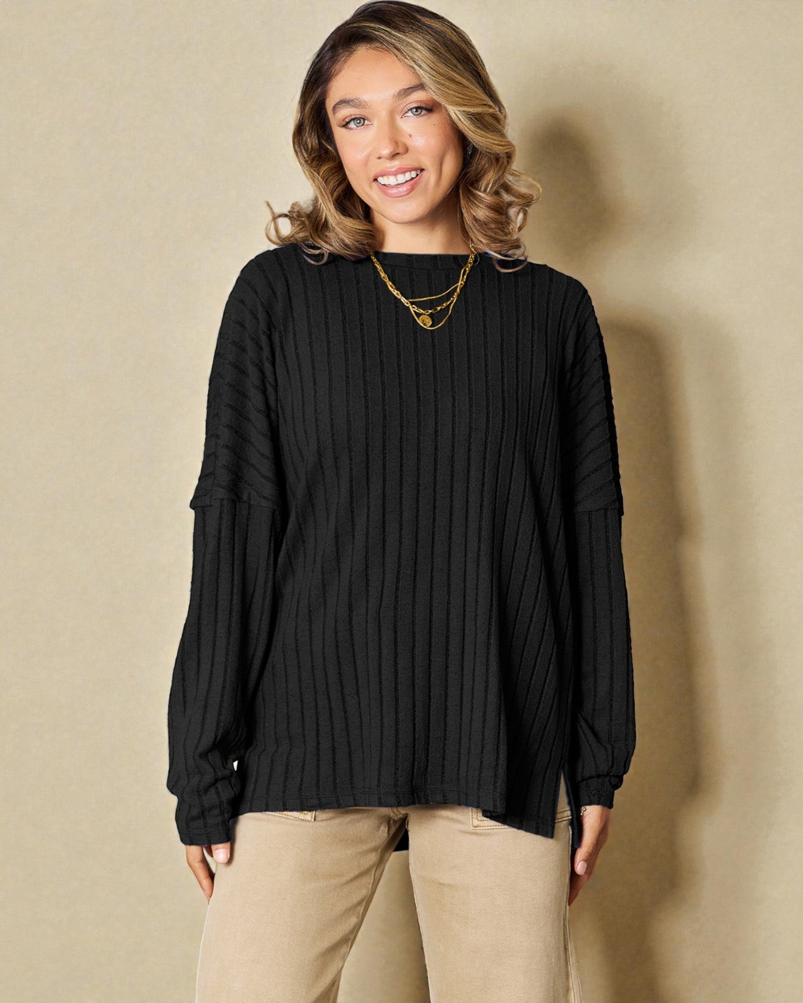 Woman wearing a black ribbed sweater and beige pants against a beige background