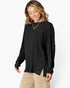 A woman wearing a black ribbed knit long-sleeve top with a high neckline and side slit, paired with beige pants, against a plain white background.