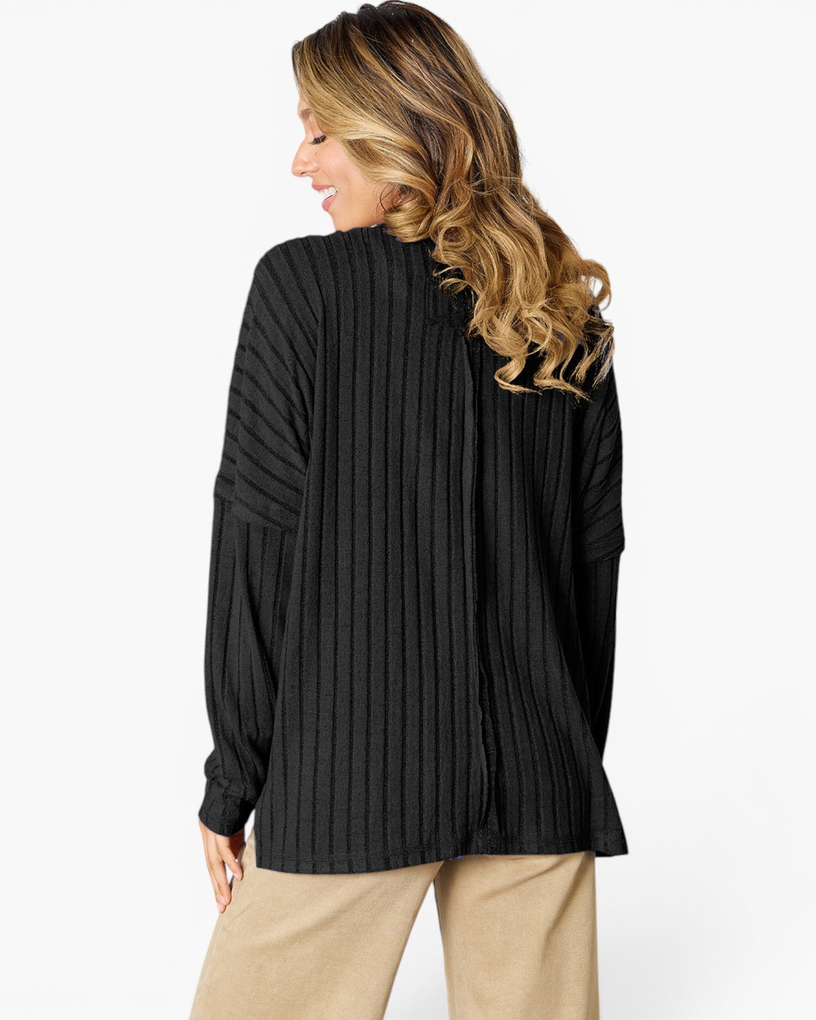 A woman shown from the back wearing a black ribbed knit long-sleeve top and beige pants against a plain white studio background.
