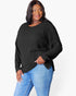 A woman modeling a black ribbed knit long-sleeve top with a boat neckline, paired with blue jeans, against a plain white studio background.