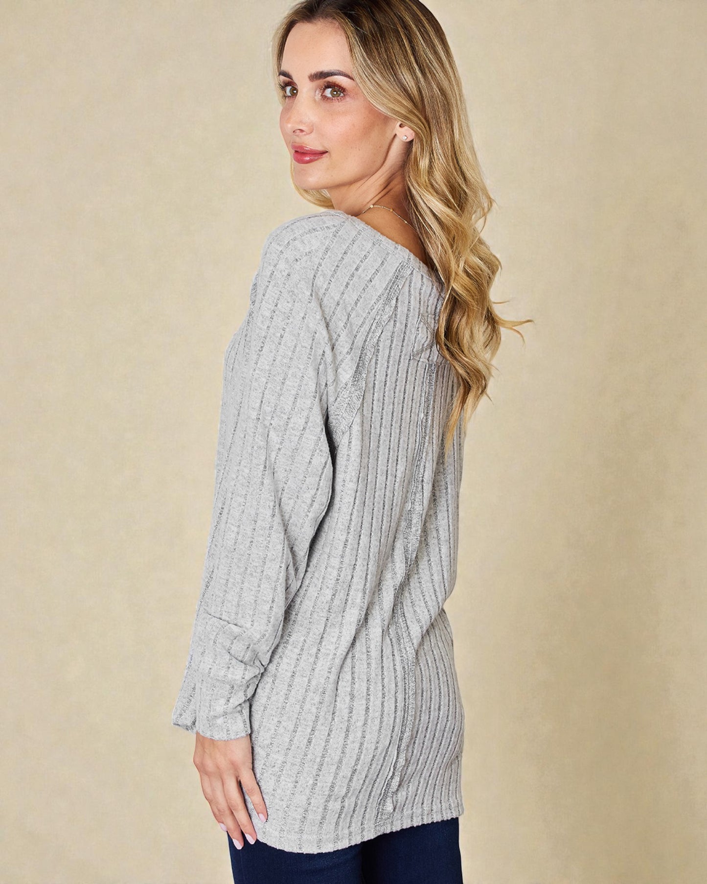 Woman wearing a gray ribbed sweater against a beige background