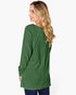 A woman with blonde wavy hair is shown from the back wearing a green long-sleeve top with vertical pleats, paired with dark blue jeans, against a plain white background.