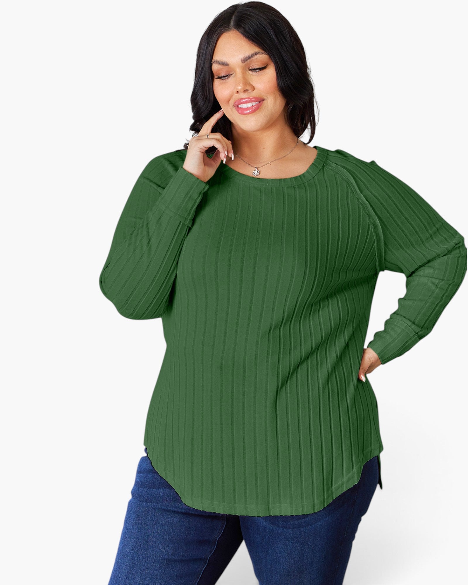 A woman modeling a green long-sleeve ribbed knit top with a crew neck and side slits, paired with blue jeans, against a plain white background.