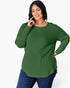 A woman modeling a green long-sleeve ribbed knit top with a crew neck and side slits, paired with blue jeans, against a plain white background.