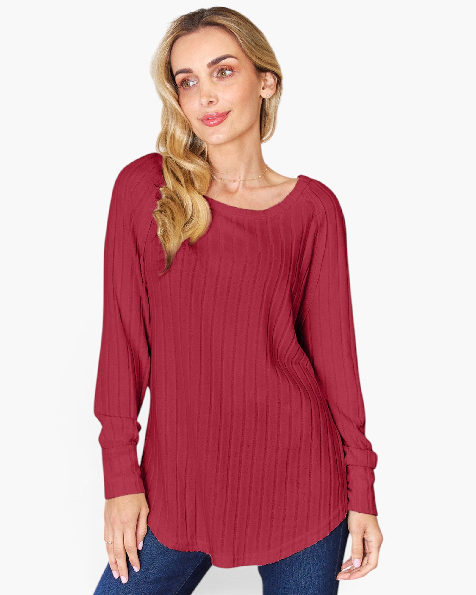 A woman wearing a long-sleeve, ribbed knit tunic top in a deep burgundy red, paired with blue jeans, against a plain light gray background.