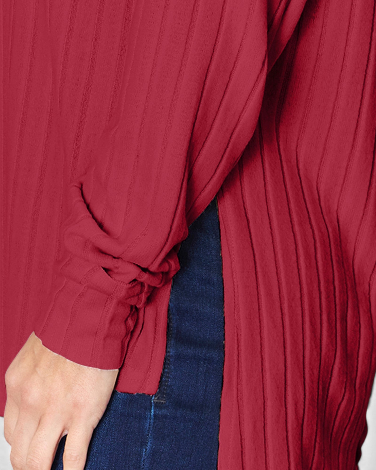 Close-up of a person wearing a pleated long-sleeve top in deep red, with the sleeve tied at the cuff and dark blue jeans visible underneath.