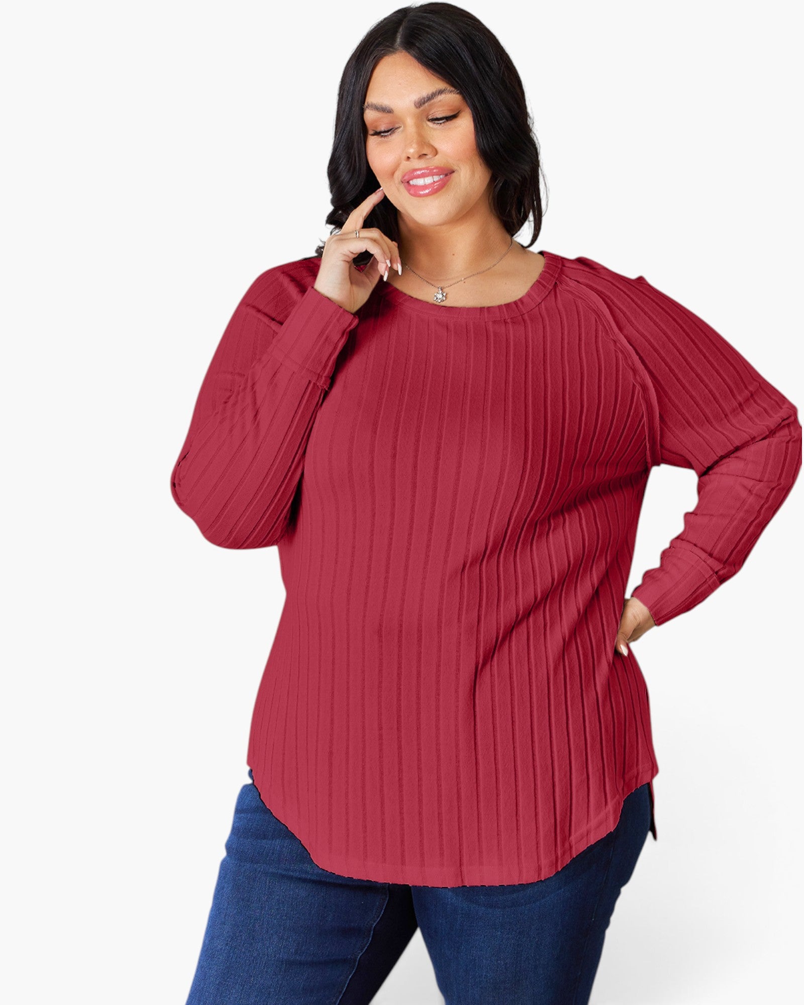 A woman wearing a ribbed long-sleeve top in a deep red or burgundy color, paired with blue jeans, against a plain white studio background.