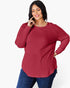 A woman wearing a ribbed long-sleeve top in a deep red or burgundy color, paired with blue jeans, against a plain white studio background.